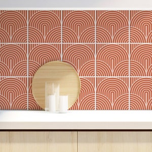 May include: A kitchen backsplash with a repeating pattern of terracotta-coloured arches outlined in white. The design is set against a white countertop and light wood cabinetry. A wooden chopping board, bowl, and cup are in the foreground.