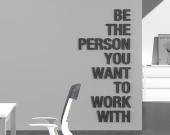 May include: Office interior with a white desk and a modern office chair with a green seat and white armrests. The wall features the text "BE THE PERSON YOU WANT TO WORK WITH" in dark gray letters.