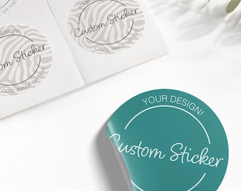 May include: A circular teal sticker with a white border and the text "YOUR DESIGN!", "Custom Sticker", and "LOGO, IMAGE OR TEXT" printed in white. A sheet of matching stickers with a grey zebra-like pattern is visible in the upper left corner.