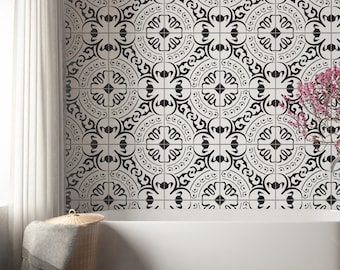 May include: A white bathtub positioned against a wall covered in square tiles featuring a repeating black and white geometric floral pattern. A brown rectangular rug lies on the floor in front of the tub, with a woven basket and a bonsai tree nearby.