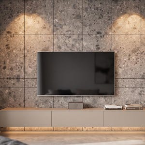 Könnte beinhalten: Ein wandmontiertes, hellbeiges, rechteckiges Medienboard unter einem Flachbildfernseher. Das Möbelstück besteht aus drei Schrankelementen und ist vor einer großen, gerasterten Wand mit grauen, gesprenkelten Steinfliesen montiert.