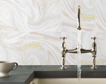 Pode incluir: Uma torneira de ponte em metal polido com dois manípulos em cruz que dispensa um fluxo constante de água para um lava-loiça branco. O fundo apresenta azulejos quadrados com um padrão de redemoinhos de mármore branco, cinzento e dourado.