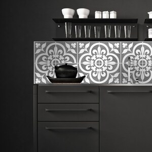 May include: Black kitchen cabinets with three drawers each, a white tiled backsplash with a floral pattern, and a black countertop.