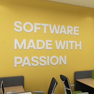 May include: A yellow office wall displaying the text "SOFTWARE MADE WITH PASSION" in white lettering. The office setting includes desks, chairs, and computer screens.