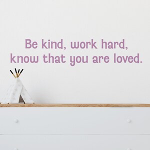 May include: A white dresser with two drawers and wooden trim, featuring a decorative teepee and the text "Be kind, work hard, know that you are loved" in lavender. The dresser has white legs and round knobs.