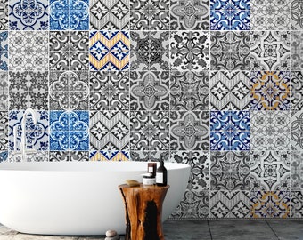May include: A white freestanding bathtub sits in front of a wall covered in square tiles featuring a variety of intricate black, white, blue, and yellow geometric and floral patterns. A natural wood stump stool holds small bottles and a stone.