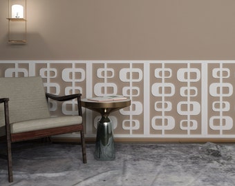 May include: A beige armchair with a wooden frame sits next to a gold and glass side table in a room with a beige wall and a white geometric patterned wainscot.