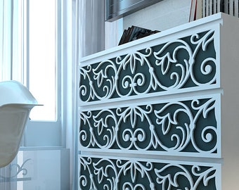 Può includere: Una cassettiera bianca a quattro cassetti con frontali grigio scuro sovrapposti da intricati motivi a volute bianchi. Accanto alla cassettiera si trova una sedia in plastica bianca stampata con gambe in legno chiaro e rinforzi in metallo nero.