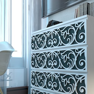 May include: A white four-drawer dresser featuring dark gray drawer fronts overlaid with intricate white scrollwork patterns. Beside the dresser stands a white molded plastic chair with light-colored wooden legs and black metal cross-bracing.