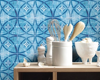 May include: A light wood kitchen console with a white ceramic utensil holder, a white textured bowl, a white pepper mill, and a whisk. The background features a wall covered in blue and white square tiles with a repeating geometric pattern.