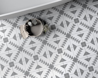 May include: A white bathtub with a black drain sits on a floor covered in square tiles featuring a repeating geometric pattern of gray triangles and squares. A small round basket containing a white cloth and a small plant sits on the tiled floor.