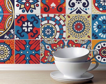 Puede incluir: Dos tazas de té de cerámica blanca apiladas con sus platos a juego, situadas frente a una pared cubierta de azulejos cuadrados con una variedad de coloridos patrones geométricos y florales en tonos rojos, azules, amarillos y blancos.