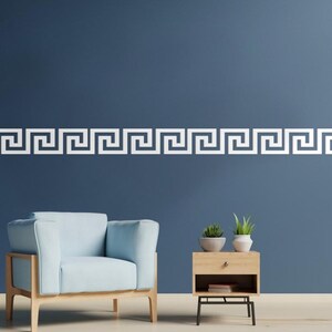 Peut inclure: Un motif de cl&eacute; grecque blanc orne le haut d'un mur bleu fonc&eacute;. En dessous, un fauteuil bleu clair avec un cadre en bois est plac&eacute; &agrave; c&ocirc;t&eacute; d'une petite table de chevet en bois avec des plantes en pot. La pi&egrave;ce a une esth&eacute;tique moderne et minimaliste.