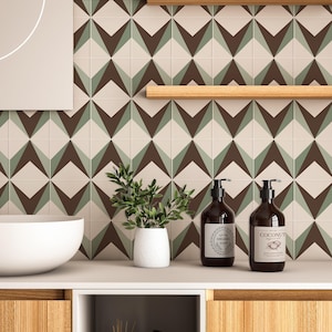 May include: A wall covered in square tiles featuring a geometric pattern of dark brown, sage green, and cream diamonds. A white ceramic basin, a small potted green plant, and two dark brown pump bottles with labels are placed on the counter.