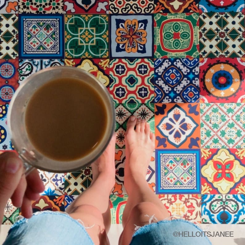 May include: A clear glass mug filled with brown coffee held in front of a floor covered in square tiles featuring a variety of colorful geometric and floral patterns in red, blue, green, yellow, and white. The text HELLOITSJANEE is visible.