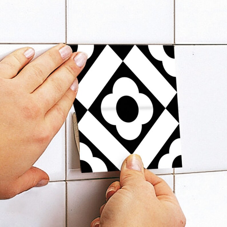 Puede incluir: Un adhesivo cuadrado para azulejos con un patr&oacute;n geom&eacute;trico en blanco y negro de alto contraste. El dise&ntilde;o consiste en una flor central de cuatro p&eacute;talos rodeada de rayas diagonales y detalles redondeados en las esquinas, aplicado sobre una superficie de azulejos blancos.