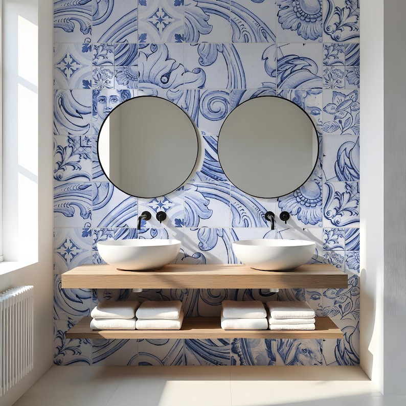 Op de afbeelding: Een badkamermeubel met twee witte waskommen op een zwevende plank van licht hout, met een onderste plank met witte handdoeken. Twee ronde spiegels met een zwart frame hangen aan een muur met blauw-witte keramische tegels.
