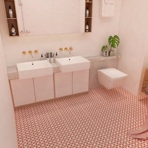 K&ouml;nnte beinhalten: Ein Badezimmer mit einem Doppelwaschtisch mit wei&szlig;en rechteckigen Waschbecken, goldenen Wandarmaturen und wei&szlig;en Schr&auml;nken. Der Boden ist mit orange-wei&szlig; gemusterten Fliesen ausgelegt. Ein Wand-WC und ein Spiegel mit Seitenregalen sind vorhanden.