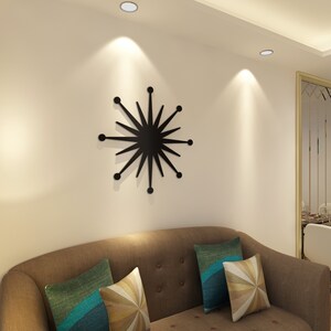 May include: A black starburst wall decor with a modern design. The decor is mounted on a white wall above a brown sofa with cushions.