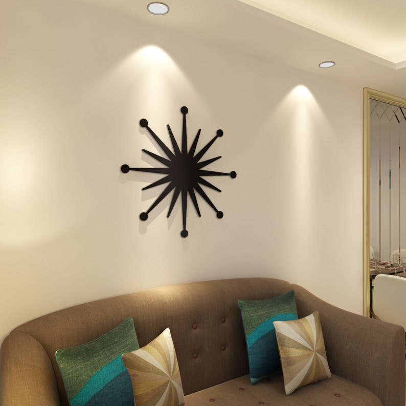 May include: A black starburst wall decor with a modern design. The decor is mounted on a white wall above a brown sofa with cushions.