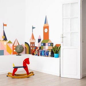 May include: A child's room with a whimsical city-themed wall mural in various colors. A red rocking horse with a yellow seat sits on the floor. A globe, books, and a potted plant are on a white shelf. A white door is on the right.