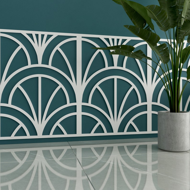 Op de afbeelding: Een wit geometrisch wandpaneel met een teal achtergrond. Het paneel heeft een herhalend patroon van overlappende bogen en waaiervormige vormen. Op de voorgrond staat een plant in een pot met groene bladeren.