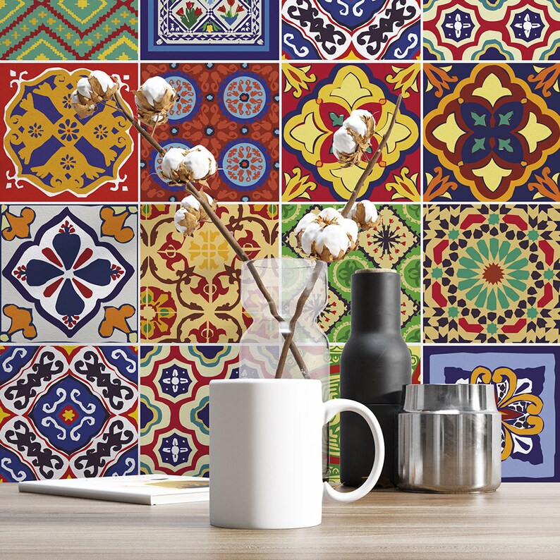May include: A white ceramic mug sits on a wooden surface in front of a wall covered in colorful, patterned square tiles. A clear glass vase holds dried cotton stems, next to a matte black bottle and a metallic silver cylindrical container.