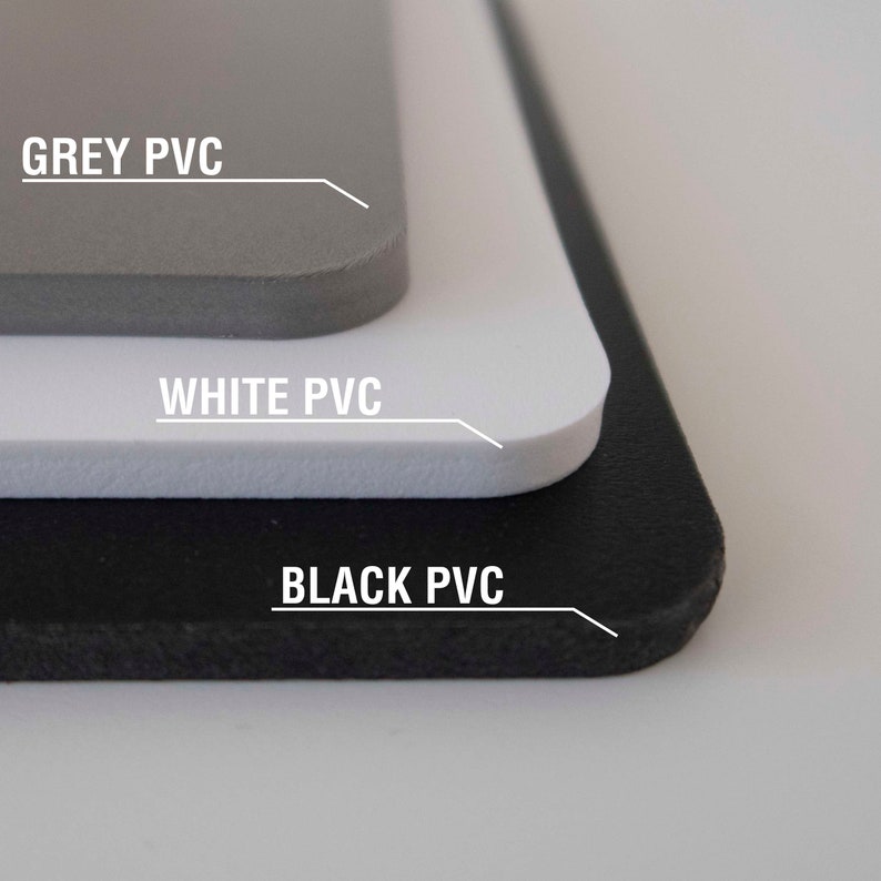 May include: A layered composition of three PVC sheets in grey, white, and black. The text "GREY PVC", "WHITE PVC", and "BLACK PVC" are displayed above each respective layer, with white lines pointing to the edges of each sheet.
