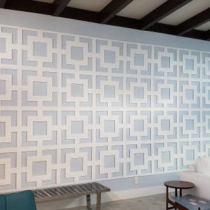 May include: A white geometric wall panel with a repeating pattern of squares and rectangles. The panel is mounted on a light blue wall.