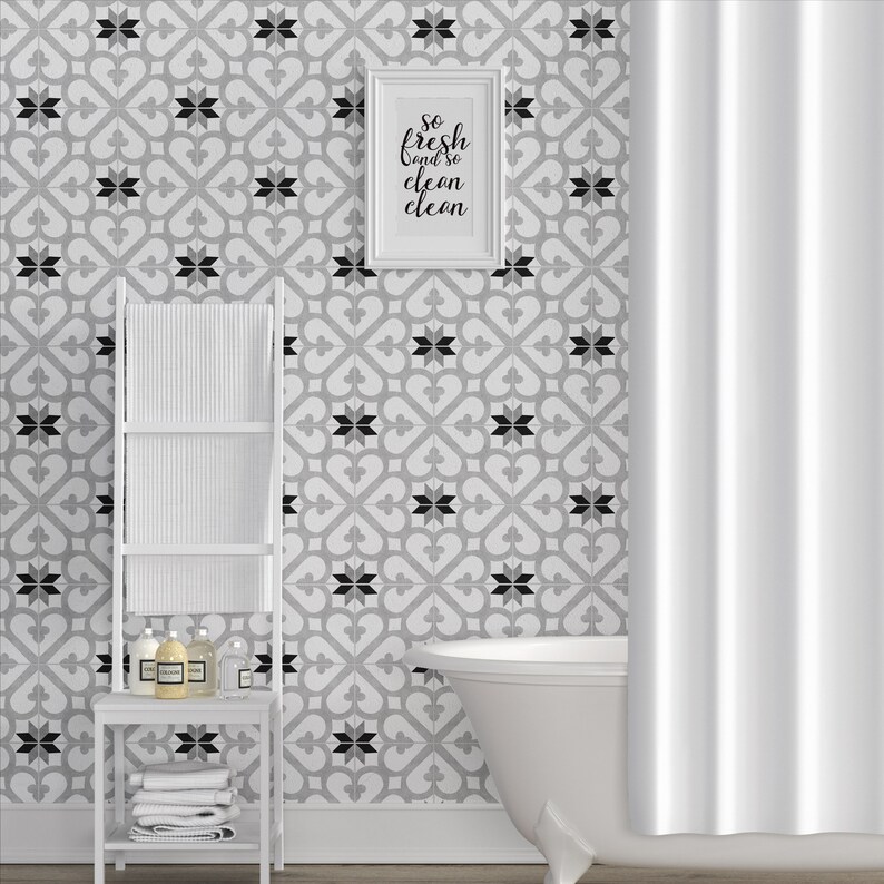 May include: A bathroom scene featuring a white freestanding bathtub, a white ladder-style towel rack with folded white towels, and toiletries. The wall has a gray and white geometric tile pattern with a framed sign reading so fresh and so clean clean.