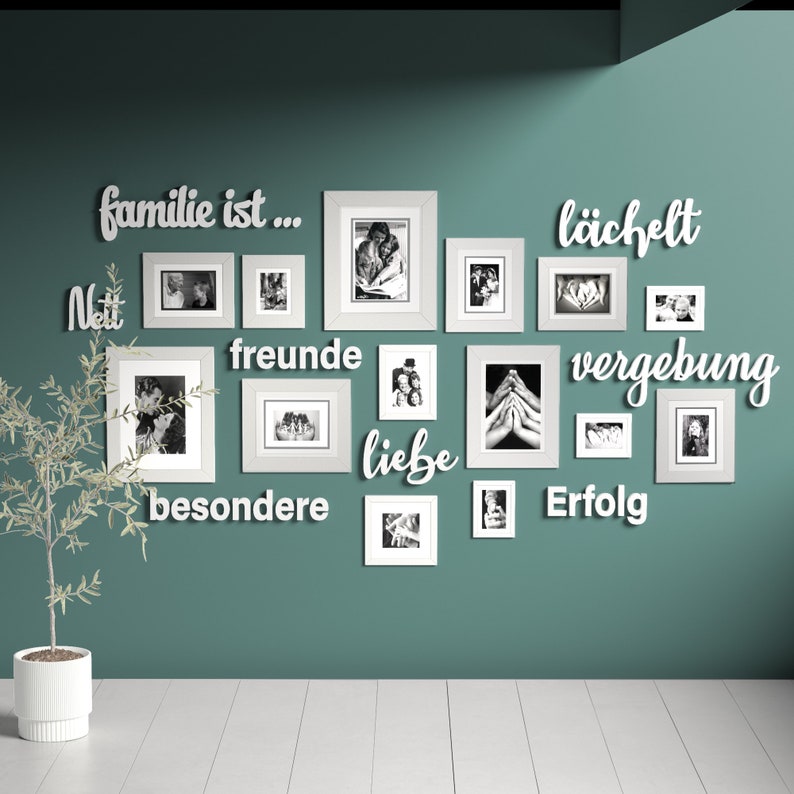 Puede incluir: Una pared turquesa con una pared de galer&iacute;a de marcos de fotos blancos. Los marcos est&aacute;n dispuestos en un patr&oacute;n aleatorio y contienen fotos en blanco y negro. La pared est&aacute; decorada con letras de madera blancas que deletrean la frase "familie ist...  neit freunde liebe besondere lachfelt vergebung erfolg".