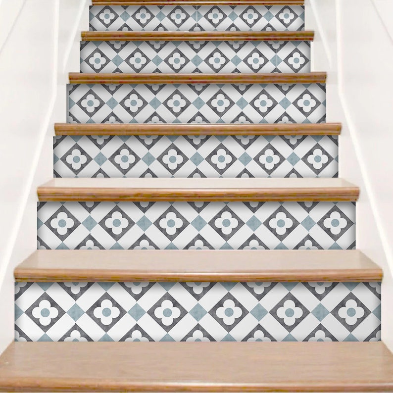 K&ouml;nnte beinhalten: Eine Treppe mit dekorativen Aufklebern f&uuml;r die Setzstufen in einem sich wiederholenden geometrischen Muster. Das Design besteht aus wei&szlig;en, dunkelgrauen und hellblauen Quadraten in einem Raster, wobei jedes Quadrat ein vierbl&auml;ttriges Blumenmotiv zeigt.