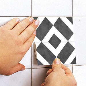 May include: A square tile decal featuring a geometric pattern of dark gray diamonds and white stripes. The decal is being applied to a white tiled surface, showing a repeating motif of intersecting lines and shapes in a high-contrast monochrome color scheme.