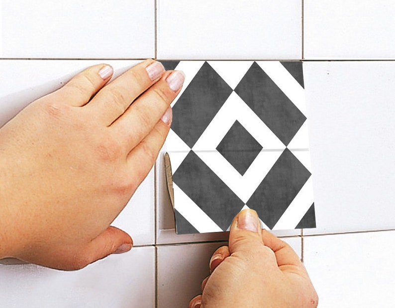 May include: A square tile decal featuring a geometric pattern of dark gray diamonds and white stripes. The decal is being applied to a white tiled surface, showing a repeating motif of intersecting lines and shapes in a high-contrast monochrome color scheme.