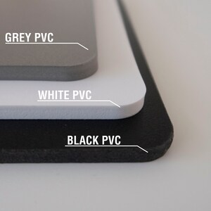 May include: Close-up of three sheets of PVC material, stacked on top of each other. The top sheet is grey, the middle sheet is white, and the bottom sheet is black. Each sheet has the text "GREY PVC", "WHITE PVC", and "BLACK PVC" printed on it.
