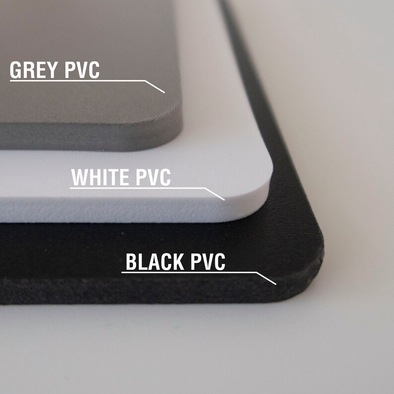 May include: Close-up of three sheets of PVC material, stacked on top of each other. The top sheet is grey, the middle sheet is white, and the bottom sheet is black. Each sheet has the text "GREY PVC", "WHITE PVC", and "BLACK PVC" printed on it.