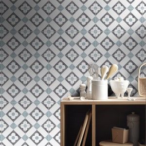 K&ouml;nnte beinhalten: Eine Wand mit quadratischen Fliesen, die ein sich wiederholendes geometrisches Muster aus wei&szlig;en vierbl&auml;ttrigen Bl&uuml;ten auf dunkelgrauen Quadraten zeigen, akzentuiert durch hellblaue Rauten. Die Fliesen bilden ein einheitliches Gittermuster.