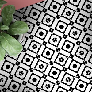 Puede incluir: Una superficie de suelo cubierta con baldosas cuadradas que presentan un patr&oacute;n geom&eacute;trico repetitivo en blanco y negro. Cada baldosa muestra un c&iacute;rculo negro central rodeado por una forma de flor blanca de cuatro p&eacute;talos en una cuadr&iacute;cula.