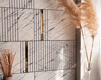 May include: A decorative wall panel with a marble-like pattern, accented by black lines and gold-colored vertical strips. The image also features tall, dried ornamental grasses in a clear vase and a small vase with dried grass.