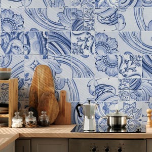 Op de afbeelding: Een aanrecht met een zilveren mokkapot, een roestvrijstalen pan, drie glazen potten met deksels en drie houten snijplanken in verschillende vormen. De muur achter het aanrecht is bedekt met vierkante tegels met blauwe bloemmotieven.