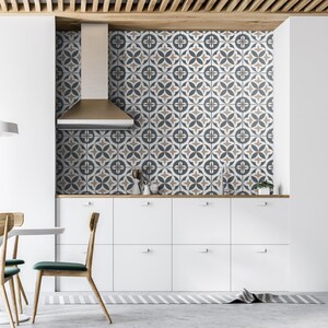 Puede incluir: Un salpicadero de cocina con azulejos cuadrados que presentan un patr&oacute;n geom&eacute;trico repetitivo en tonos azul oscuro, beige y blanco. Los azulejos est&aacute;n dispuestos en cuadr&iacute;cula detr&aacute;s de una campana extractora de acero y armarios blancos.