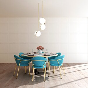 May include: A round dining table with a white marble top and gold legs. Six teal blue chairs with gold frames surround the table. A three-light pendant fixture with gold accents and white globe shades hangs above the table.