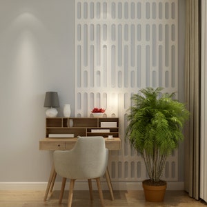 May include: A light wood desk with a matching chair, a small lamp, and decorative vases. A large green plant in a brown pot sits to the right. The wall behind the desk has a white, patterned design.