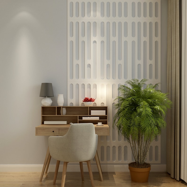 May include: A light wood desk with a matching chair, a small lamp, and decorative vases. A large green plant in a brown pot sits to the right. The wall behind the desk has a white, patterned design.