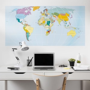 May include: A colorful world map poster hangs above a white desk. The desk holds a laptop, desk lamp, and office supplies. A small succulent plant in a black pot and a white vase are also on the desk. The map is a detailed political map.