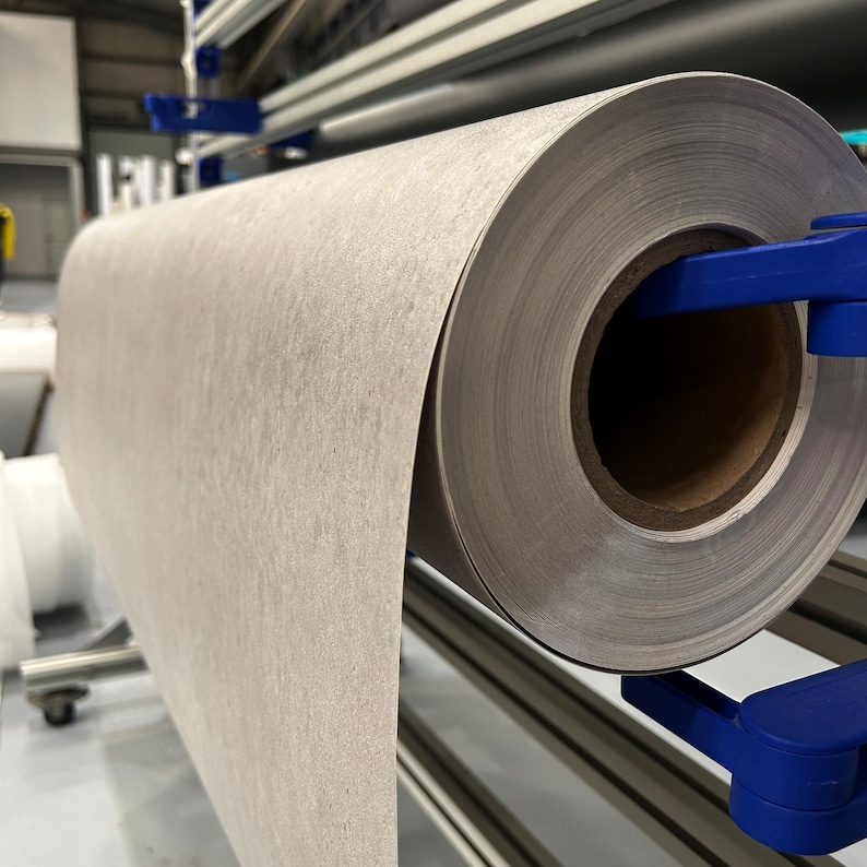 K&ouml;nnte beinhalten: Eine gro&szlig;e Rolle hellgrauen, strukturierten Materials wird von blauen Klammern gehalten. Das Material scheint Papier oder Stoff zu sein und ist auf einem Metallrahmen montiert. Die Rolle ist teilweise abgerollt und zeigt die Textur.