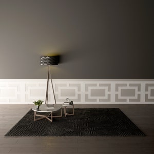 May include: A black geometric lamp with a tripod stand sits on a black and white patterned rug with two round white marble coffee tables. The tables are in front of a white wainscoting with a gray wall behind it.