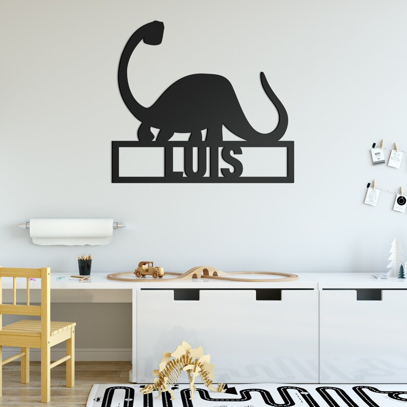 May include: Black dinosaur wall decor with the name "Luis" cut out below. The dinosaur is standing on a shelf with a white background.