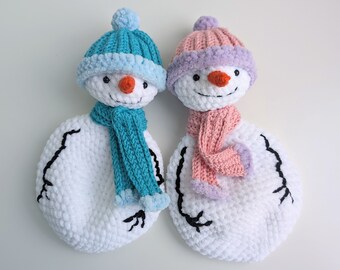 May include: Two crocheted snowmen, one with a teal hat and scarf and the other with a pink hat and scarf.