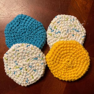 May include: Four crocheted dishcloths in different colors: blue, white with blue and green flecks, white with green and blue flecks, and yellow.